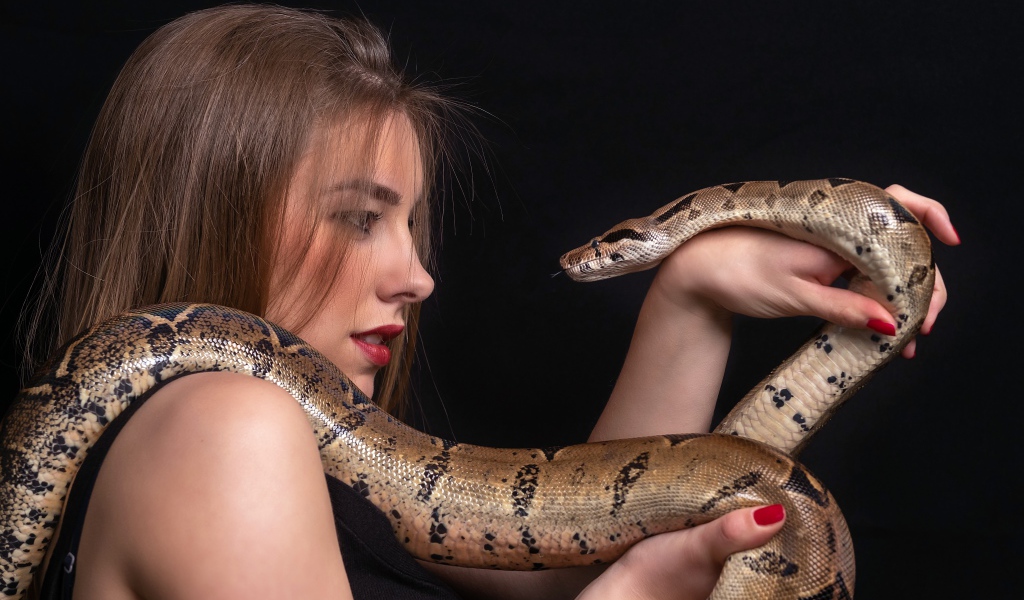 Молодая девушка со змеей в руках на черном фоне