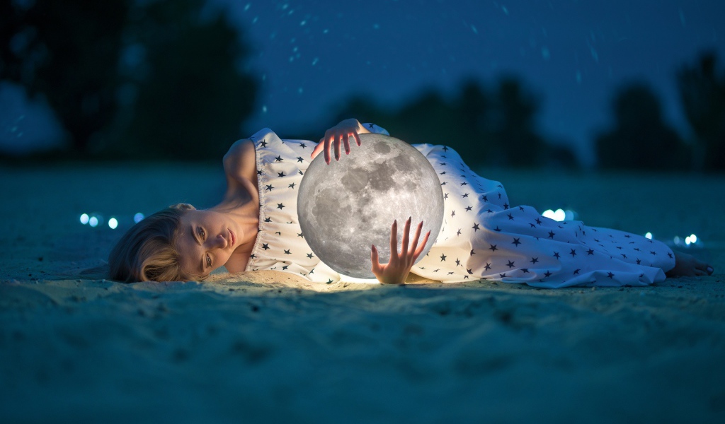 Молодая девушка с луной в руках лежит на песке