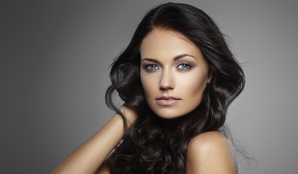 Молодая настоящая голубоглазая длинноволосая брюнетка на сером фоне