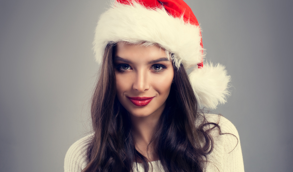 Красивая брюнетка в новогодней шапке на сером фоне