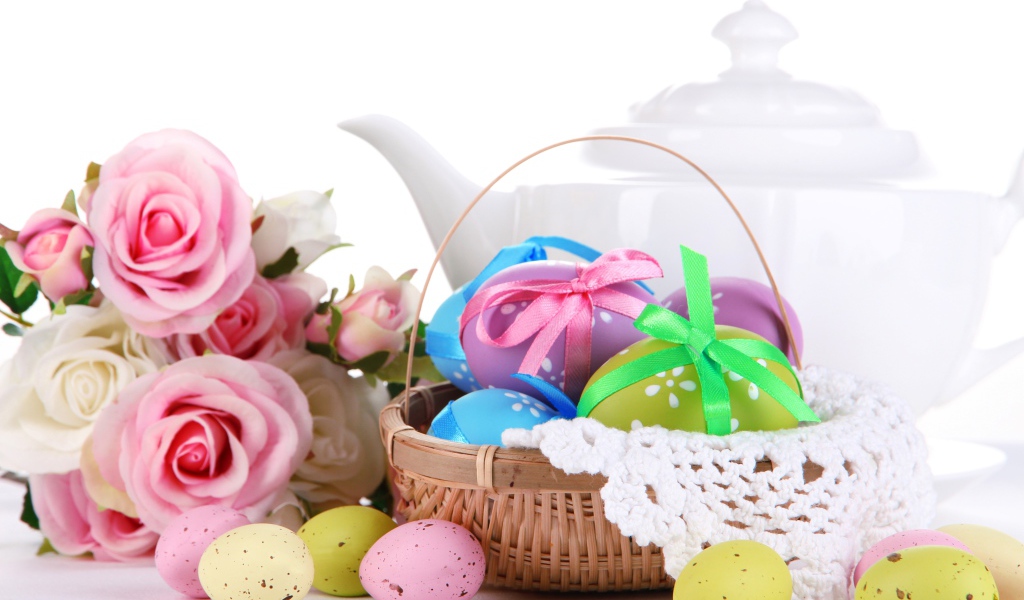 Корзина с пасхальными яйцами на столе с букетом роз и белым чайником