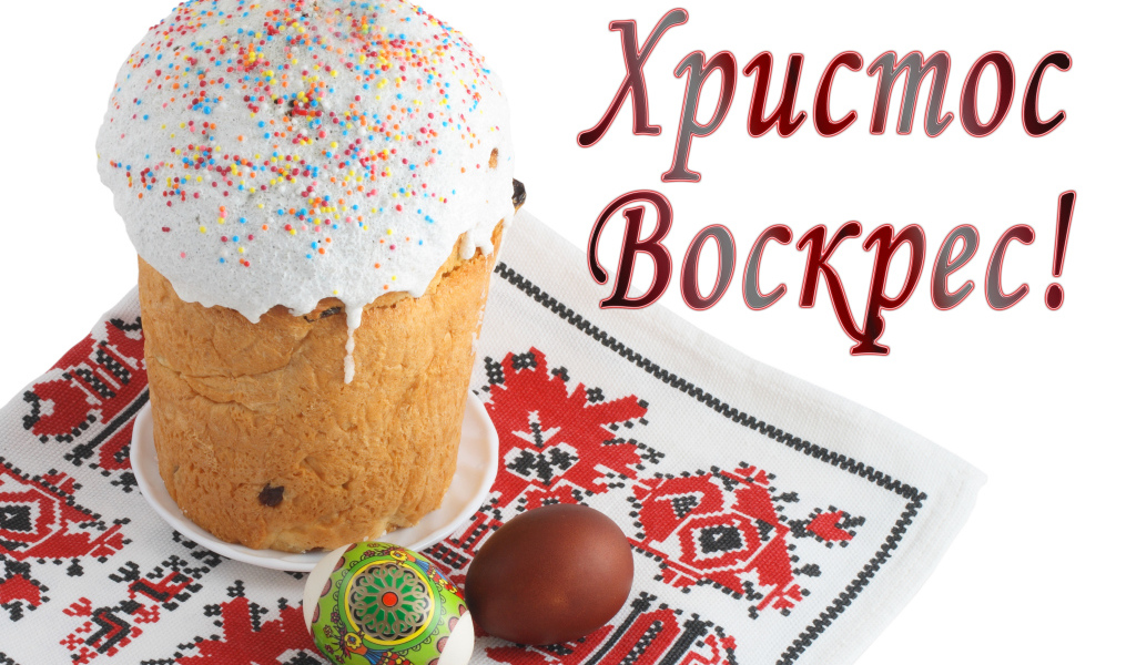Пасхальный кулич с белой глазурью и крашеными яйцами на рушнике с надписью Христос Воскрес на белом фоне
