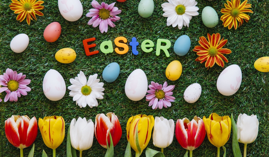 Надпись Easter на зеленой траве с крашеными яйцами и цветами