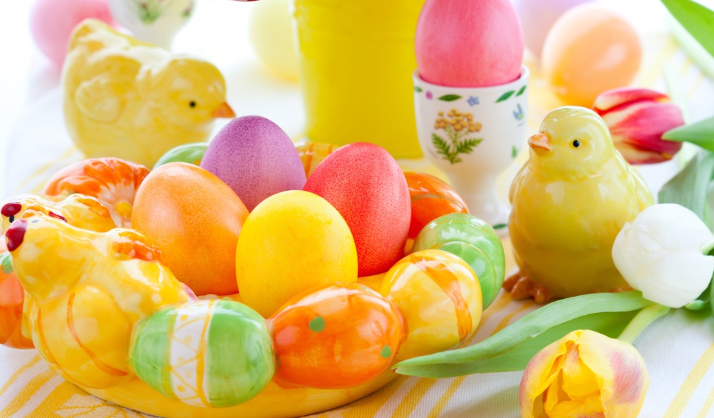 Разноцветные яйца с фигурками на столе с тюльпанами к Пасхе