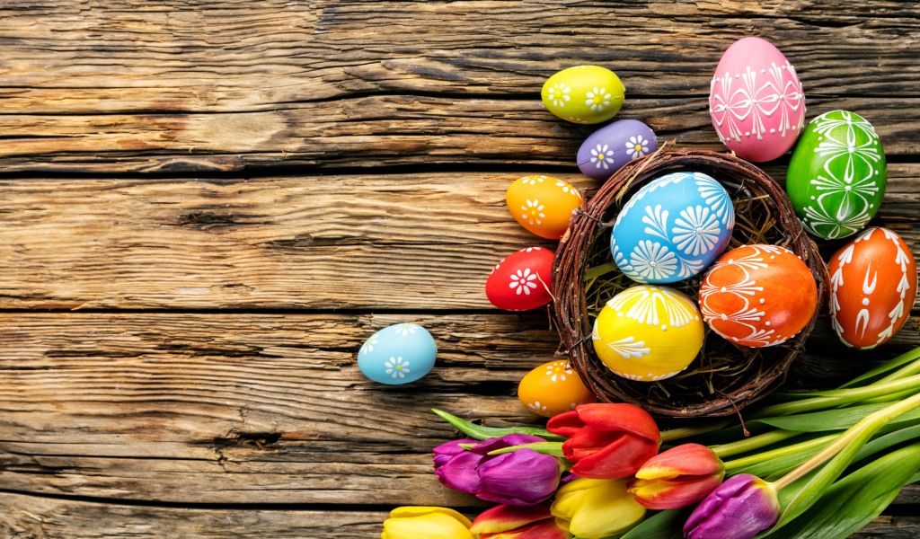 Крашеные пасхальные яйца с букетом тюльпанов на деревянном фоне