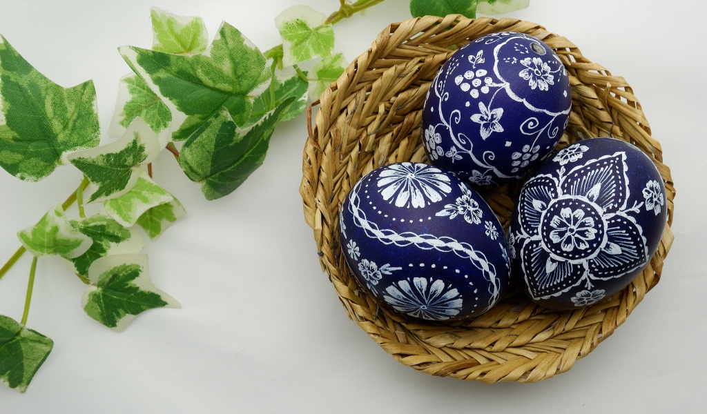 Три раскрашенных яйца в корзинке на столе с веткой 