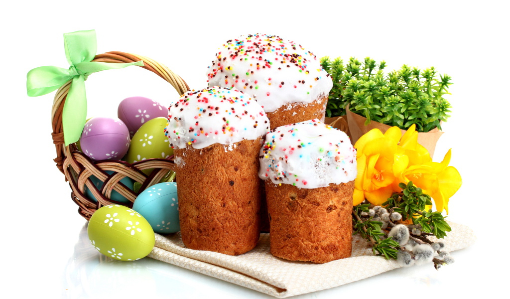Три сладких кулича на белом фоне с цветами и крашеными яйцами к празднику Пасха