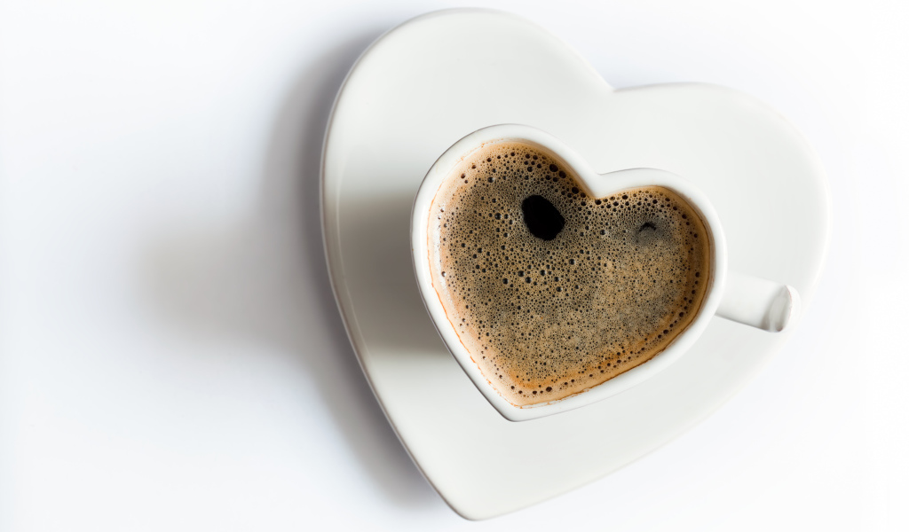 Красивая белая чашка в форме сердца с кофе на белом фоне