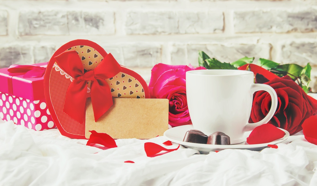 Коробка с подарком на столе с чашкой кофе и красными розами 