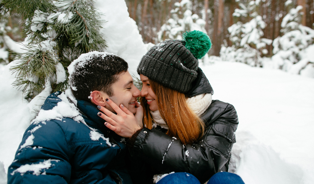 Влюбленная пара сидит под заснеженной еловой веткой зимой