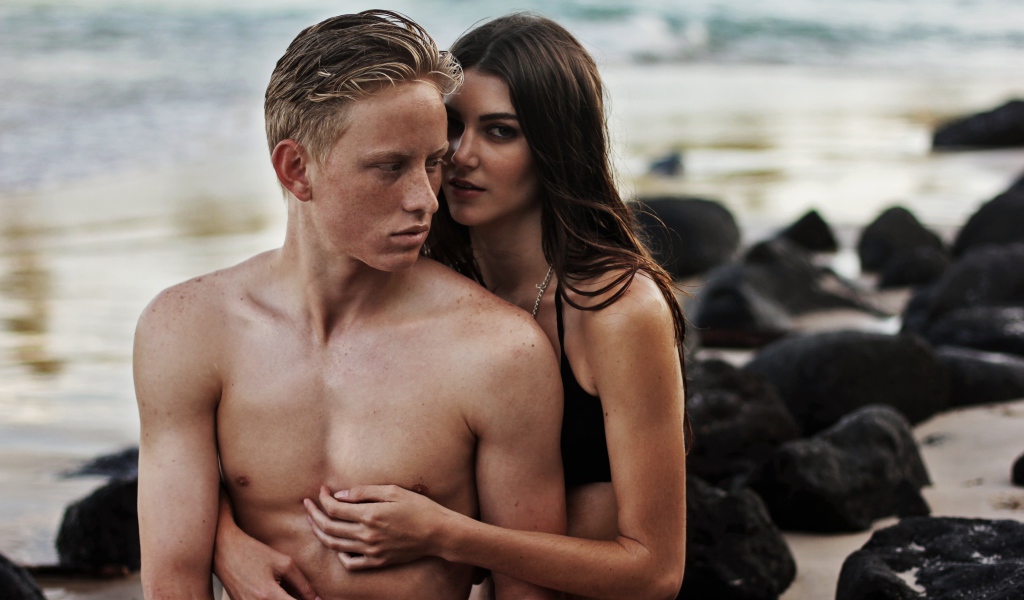 Влюбленная пара сидит на камнях на берегу моря 