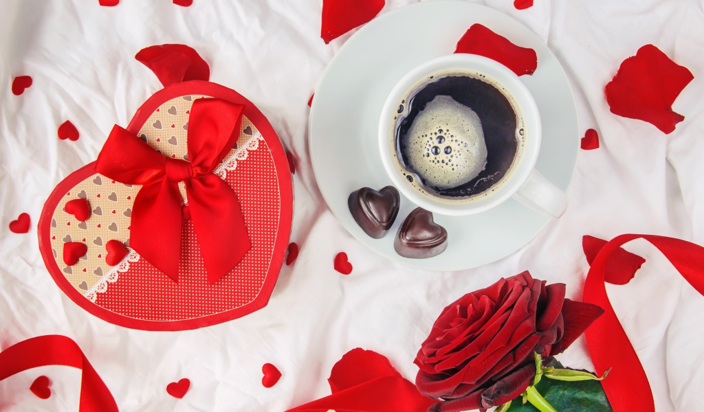 Кружка с кофе и шоколадными конфетами на столе с подарком и красной розой 