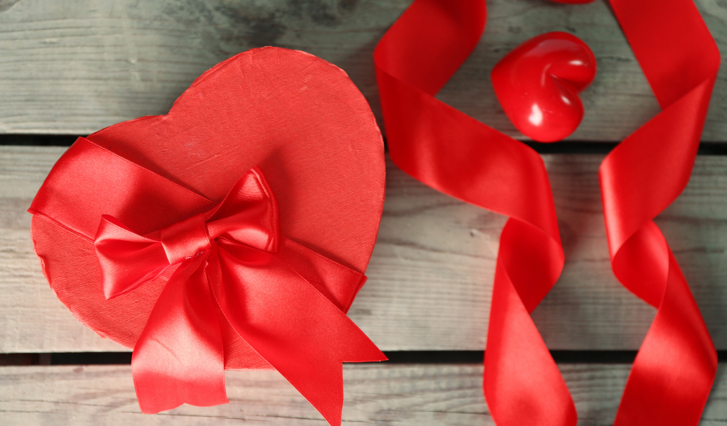 Красная коробка в форме сердца на деревянном столе с красными лентами