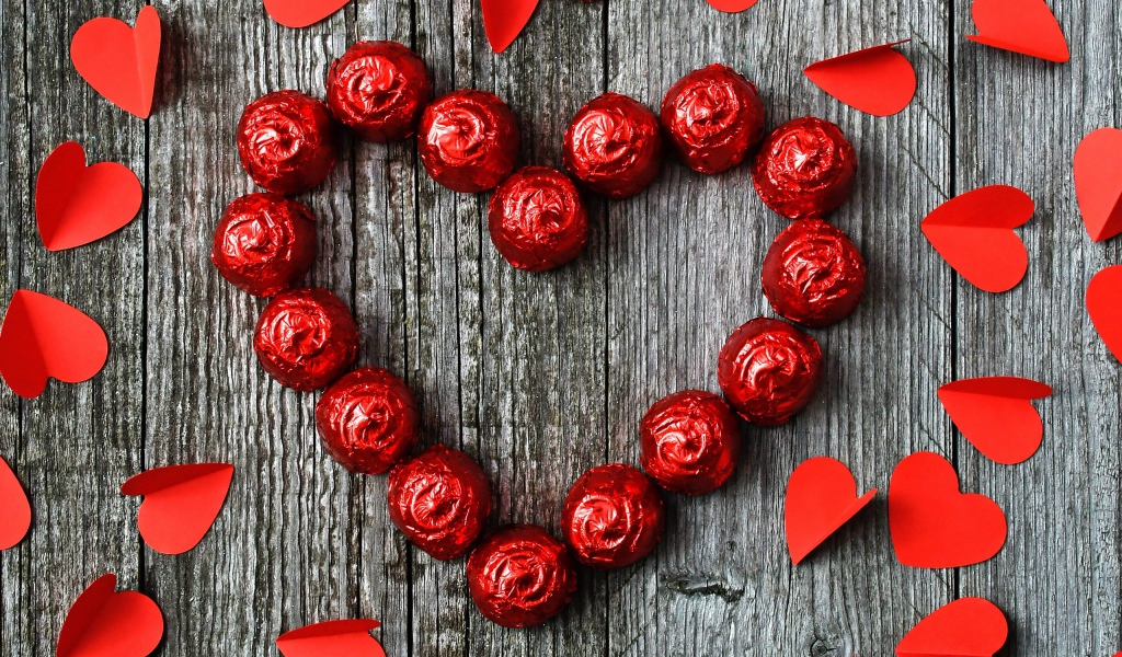 Красное сердце из конфет на деревянном фоне с бумажными сердечками