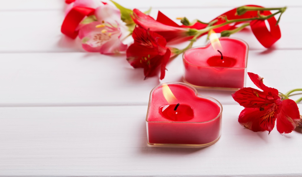 Two red heart-shaped candles on a table with alstroemeria flowers