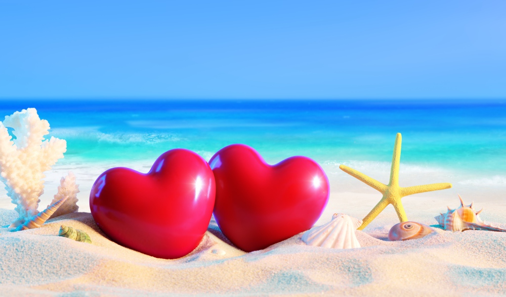 Два красных сердца на белом песке с ракушками на фоне моря
