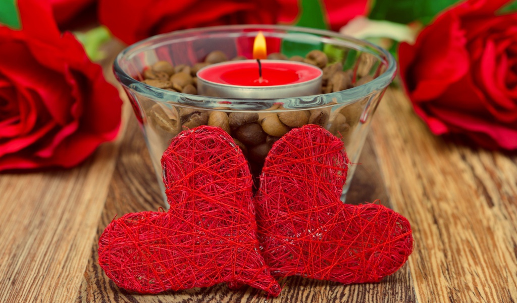 Два красных плетеных сердца на столе с зажженной свечой
