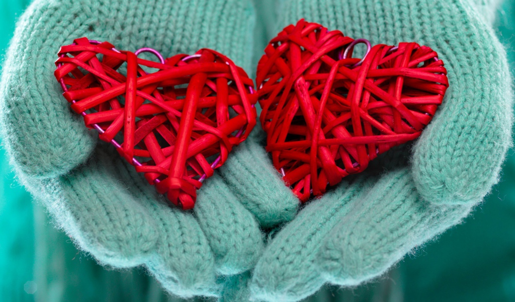 Два плетеных красных сердца лежать на руках в варежках