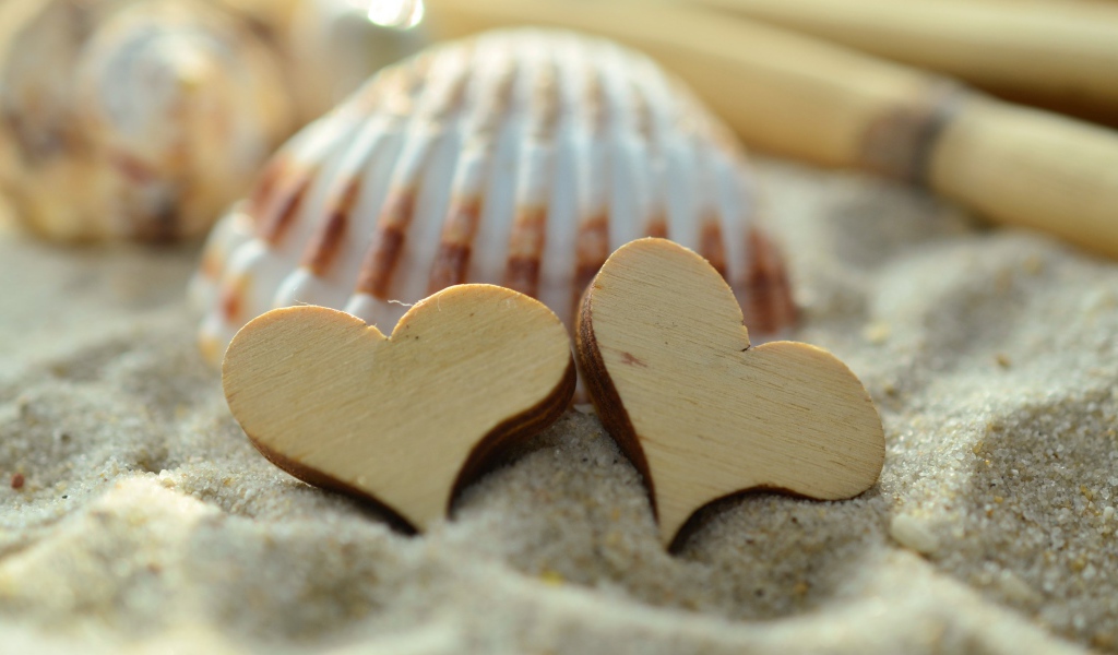 Два деревянных сердца и ракушки лежат на песке