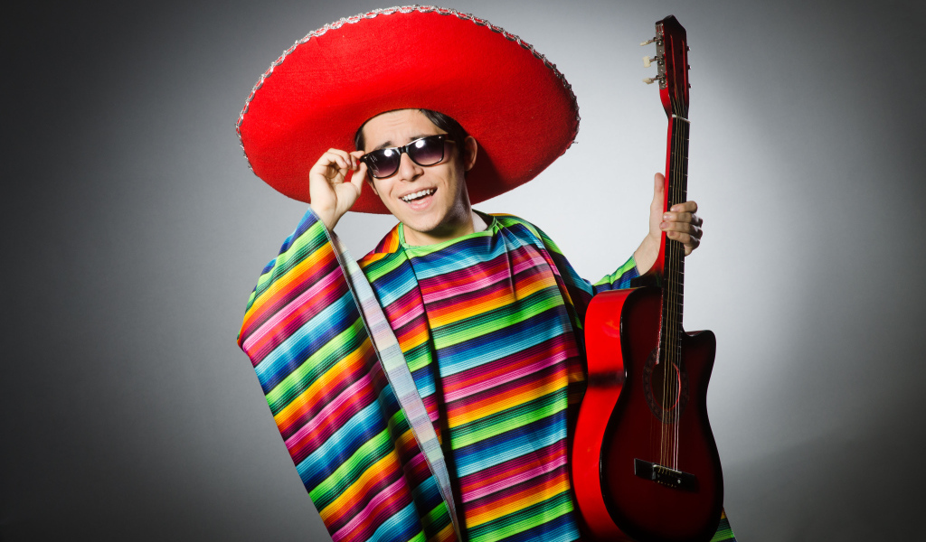 Мужчина в красном сомбреро с гитарой в руках на сером фоне