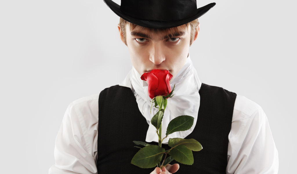 Парень в цилиндре с красной розой в руке на сером фоне