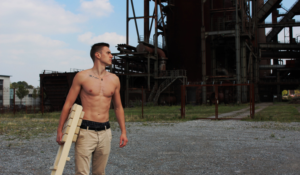 Красивый молодой парень стоит на фоне завода