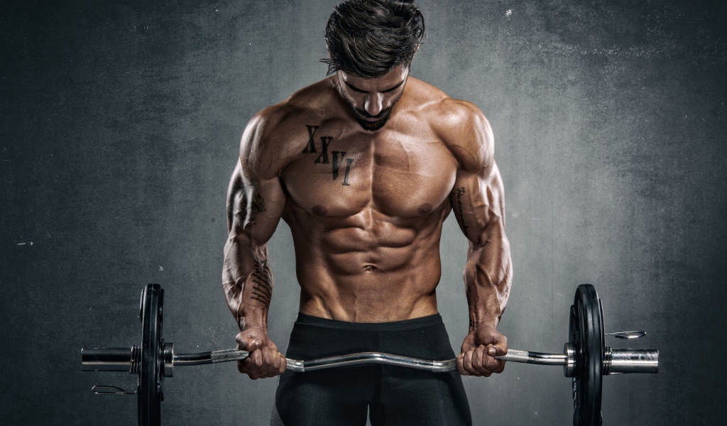 Накаченный мужчина с гантелей в руках на сером фоне