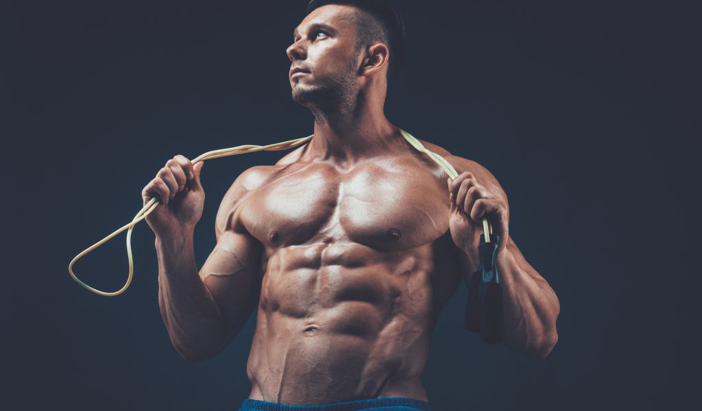 Накаченный мужчина со скакалкой в руках на сером фоне