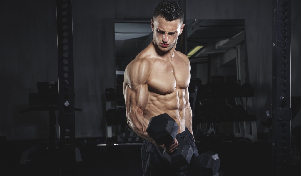 Накаченный мужчина с тяжелыми гантелями в руках 