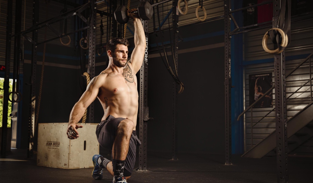 Накаченный мужчина с татуировками на теле с гантелей в руке