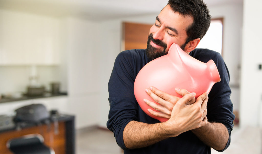 Мужчина обнимает розовую свинью копилку 