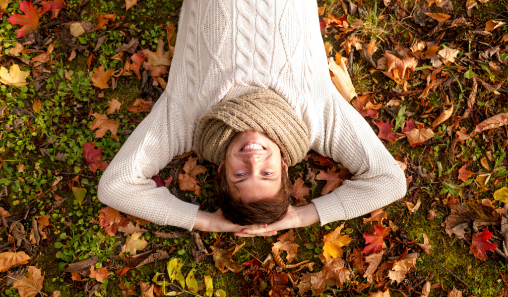 Smiling man in a sweater lies on fallen leaves