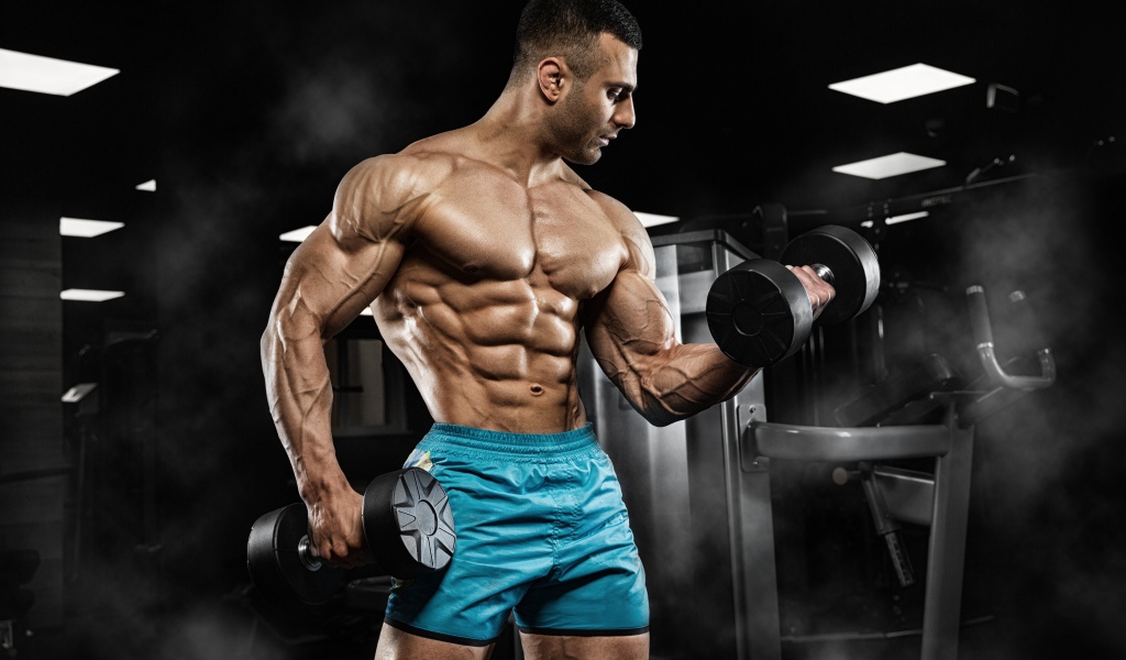Strong pumped man in shorts with dumbbells in his hands