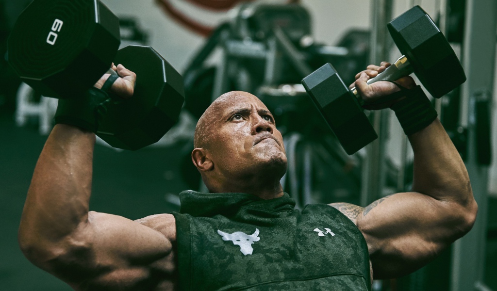 Американский актер, сильный мужчина Дуэйн Джонсон с гантелями в спортзале