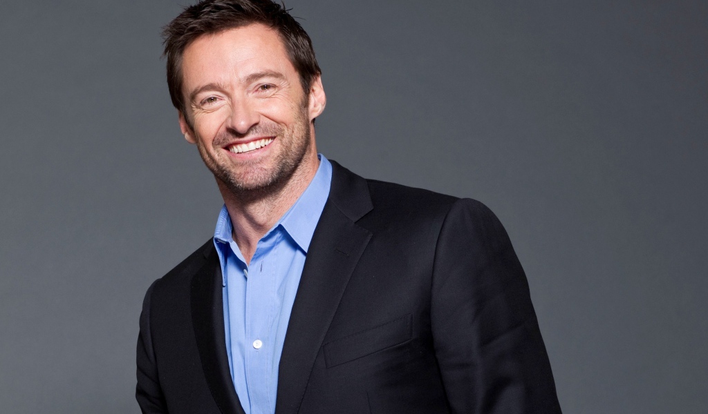 Улыбающийся мужчина, актер Хью Джекман  в костюме на сером фоне