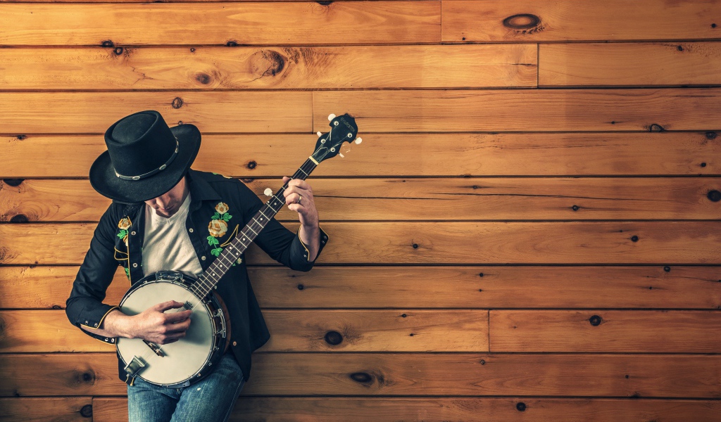 Парень музыкант играет на банджо у деревянной стены