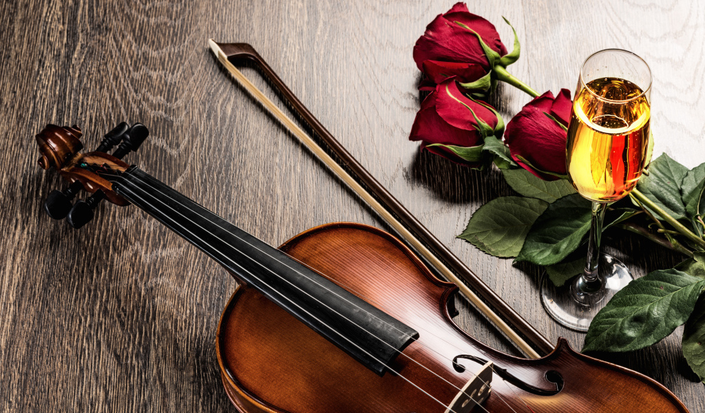 Скрипка лежит на столе с бокалом шампанского и красными розами