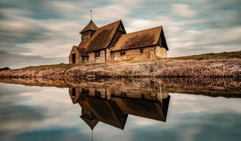 Старый дом на берегу реки отражается в воде