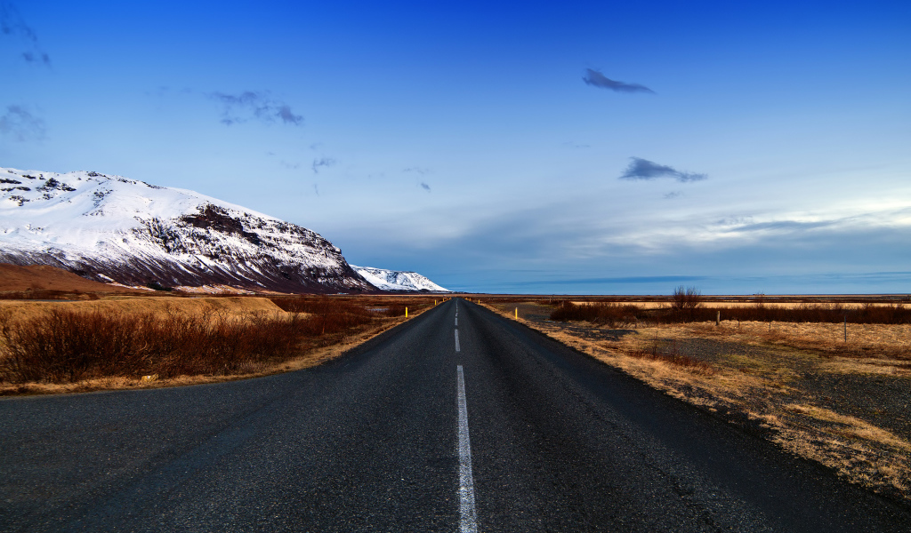 Ровная асфальтовая дорога у заснеженных гор