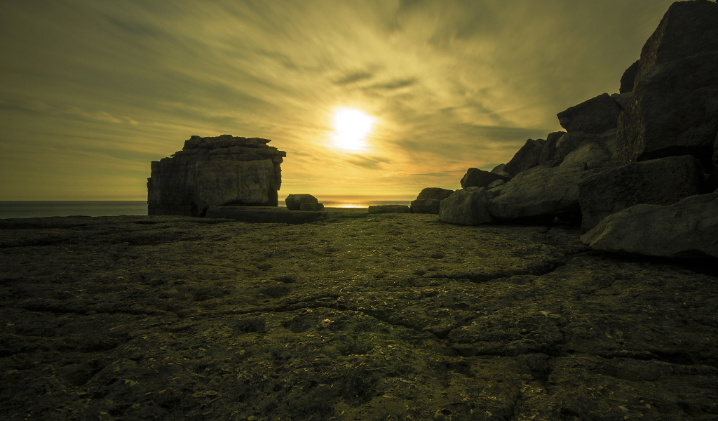 Солнце в облаках освещает камни у моря