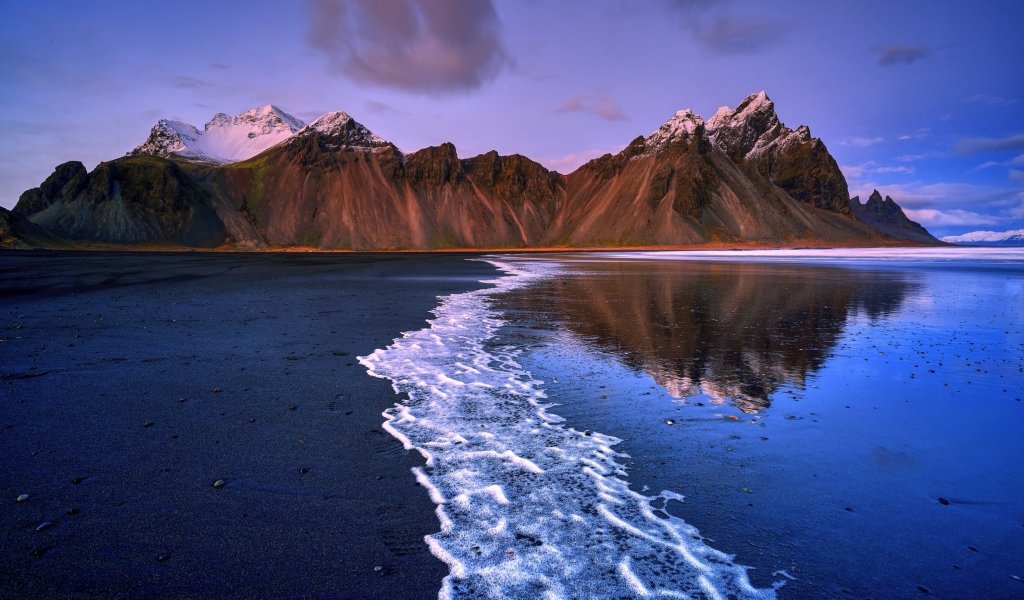 Вода на черном песке на фоне гор 