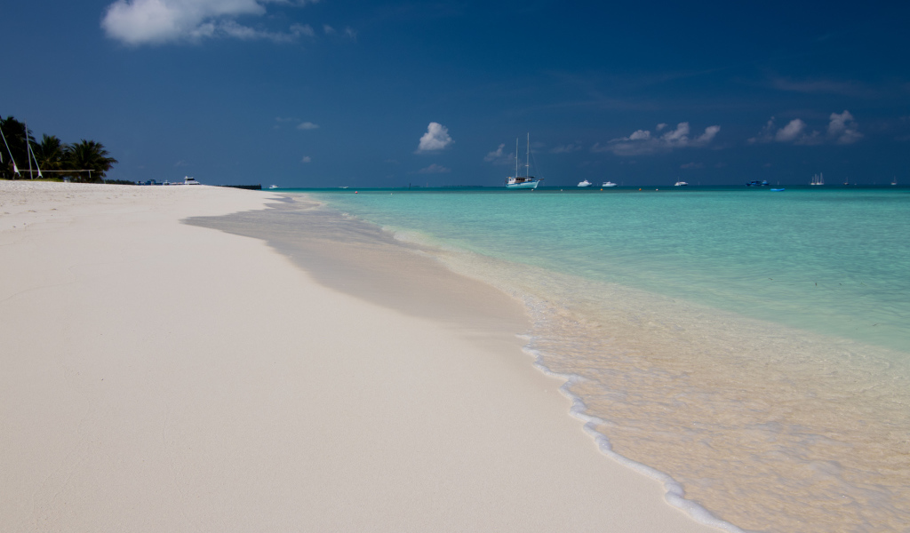 Спокойные волны на белом горячем песке под голубым небом
