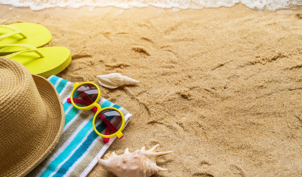 Шляпа, очки, полотенце и ракушки на желтом песке у моря