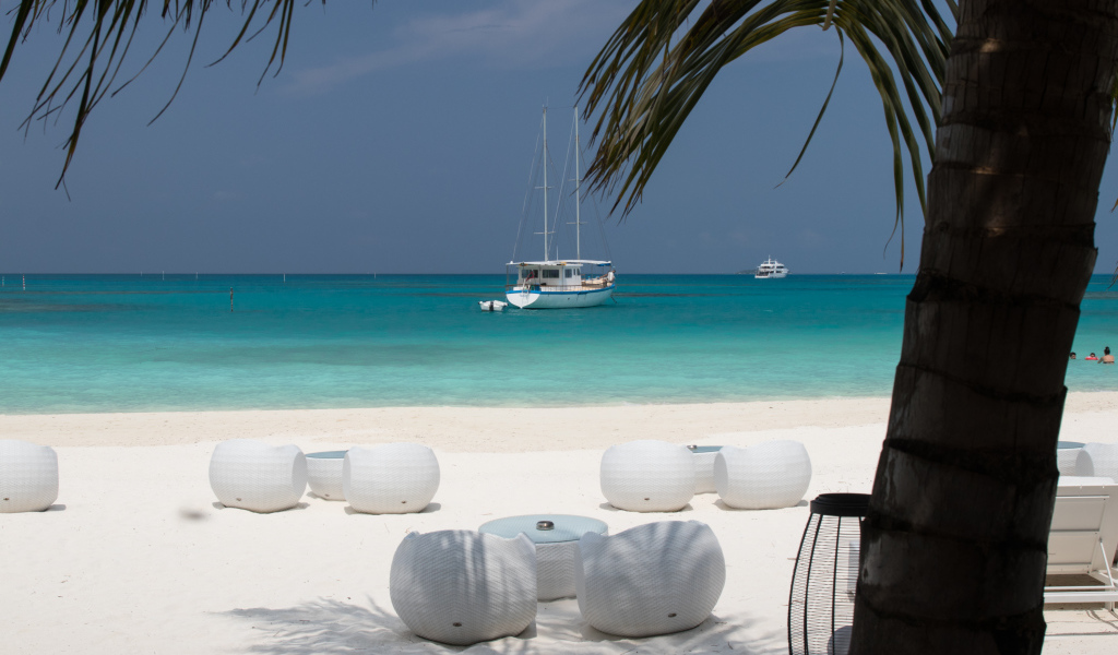 Белые кресла и столики на белом песке на пляже у голубой воды