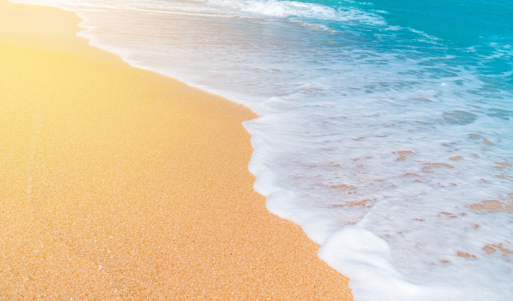 Белые волны океана омывают желтый горячий песок на пляже