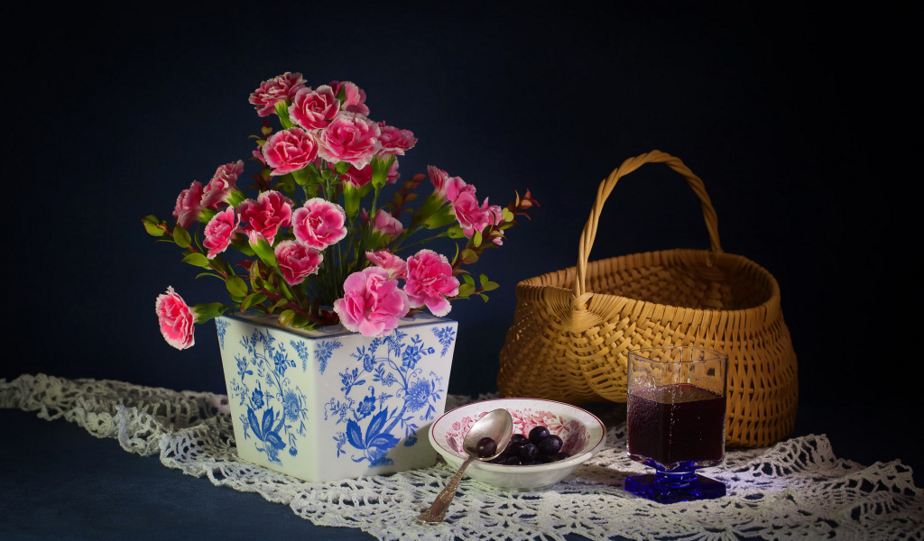 Букет гвоздик в красивой вазе на столе с корзиной и соком