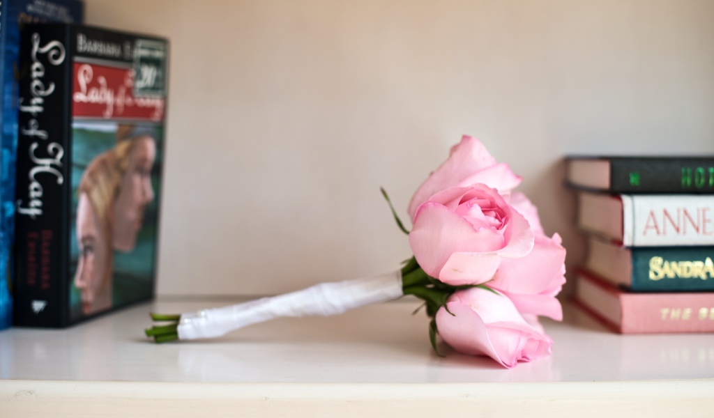 Букет розовых роз лежит на полке с книгами