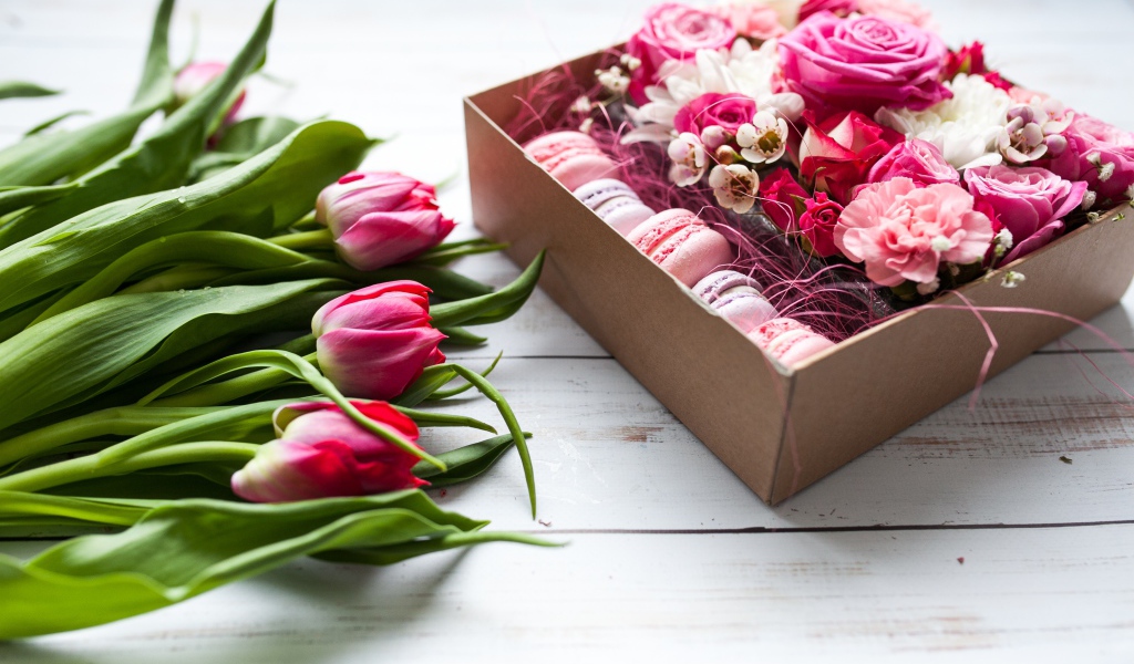 Букет розовых тюльпанов на столе с коробкой печенья макарон и цветами