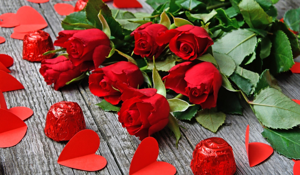 Букет красных роз на деревянном столе с конфетами и красными сердечками
