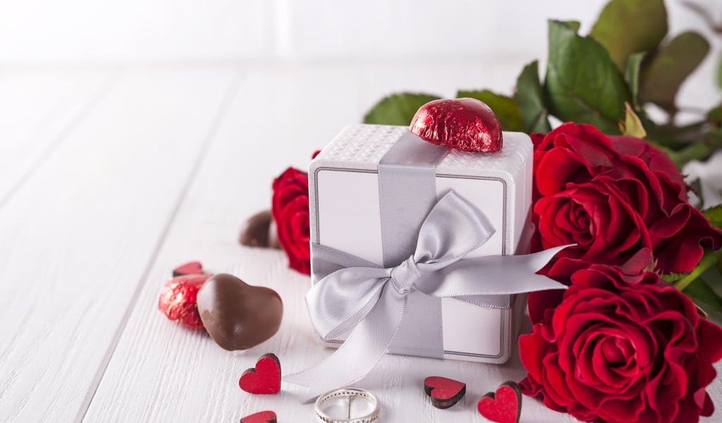 Подарок на столе с конфетами и букетом красных роз 